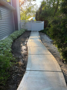 A straight-on view of the new concrete walkway with its picture frame edge, showing the sun glinting off the wet surface.