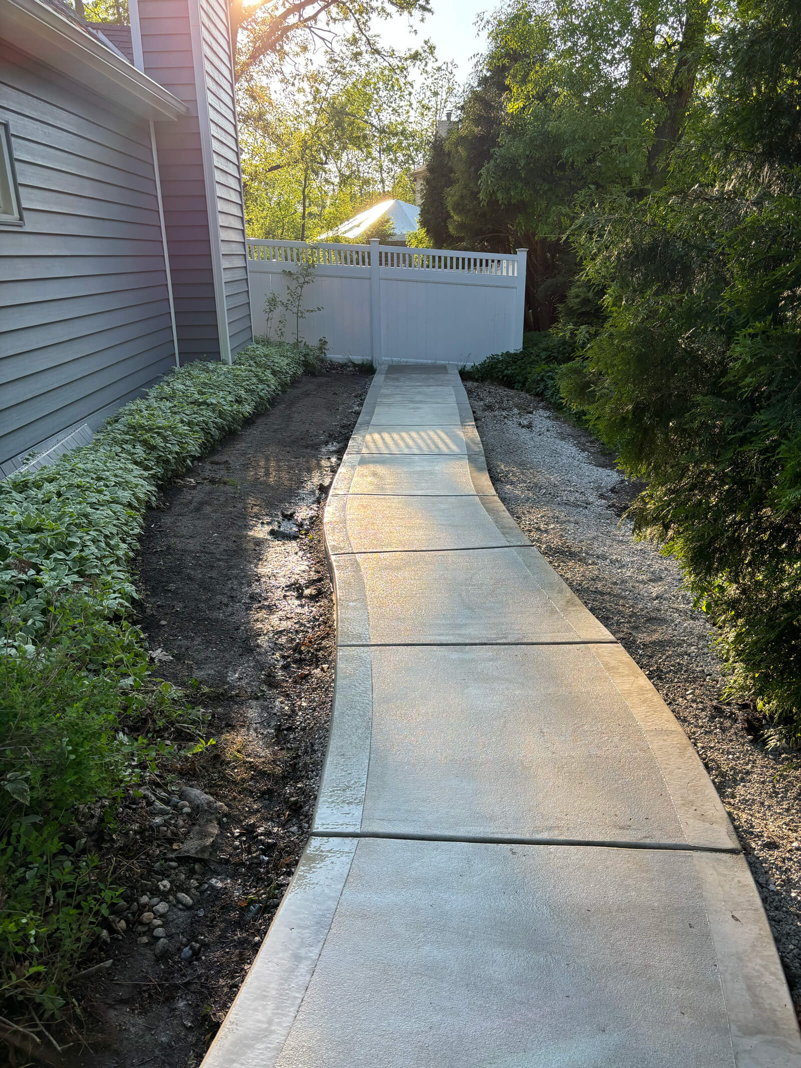 A straight-on view of the new concrete walkway with its picture frame edge, showing the sun glinting off the wet surface.