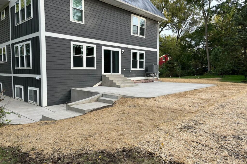 A wide view of a new concrete patio and steps installed behind a modern home in Franklin, WI, with the surrounding yard prepared for landscaping.