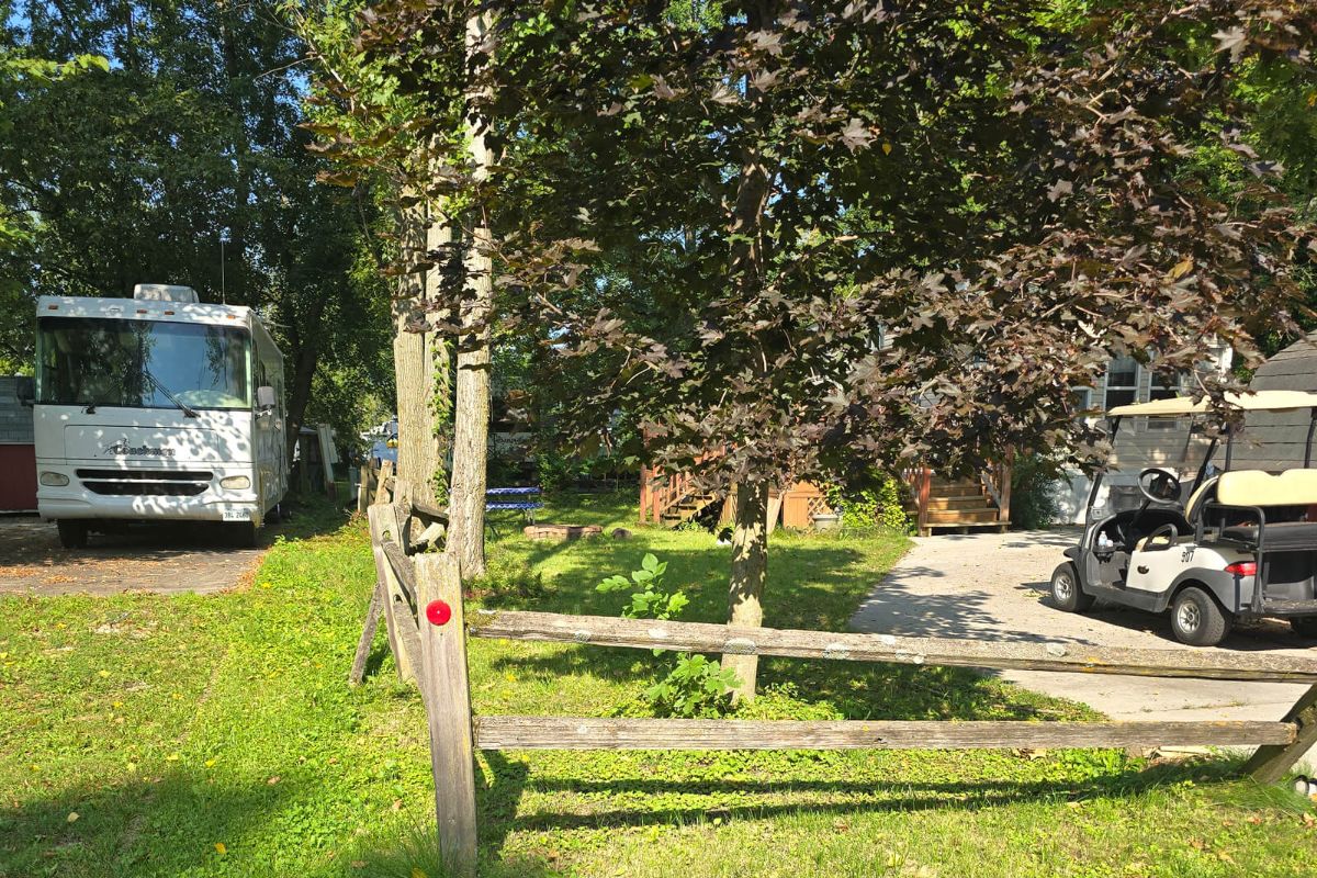A view of the RV park site, showing a split-rail fence and trees, before the start of the concrete project.