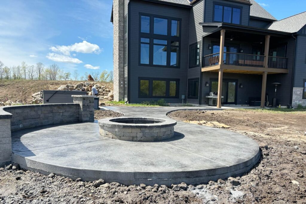 A view of the completed stamped concrete patio and walkway, showing the smooth, finished surface and surrounding landscape with a hot tub and grill.
