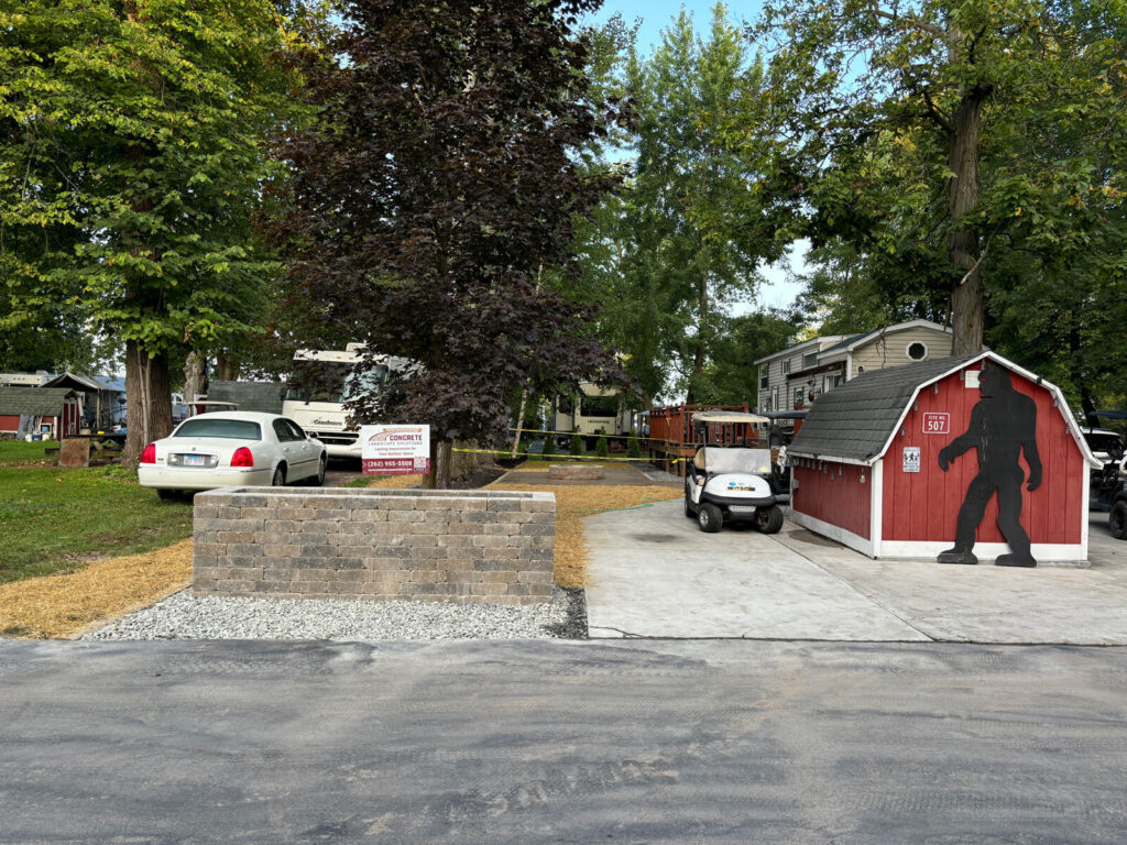 A view of the new stamped concrete patio and a retaining wall, with a small shed and a Bigfoot cutout in the background at Riverbend RV Park.
