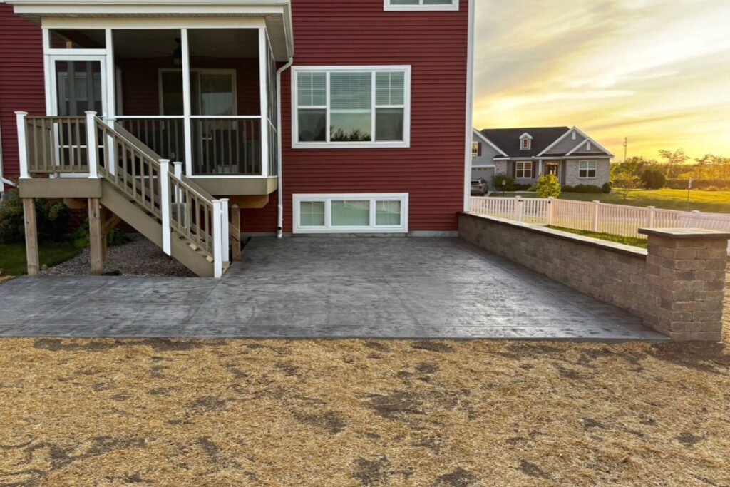 A finished stamped concrete patio with a long retaining wall and pillars at sunset.