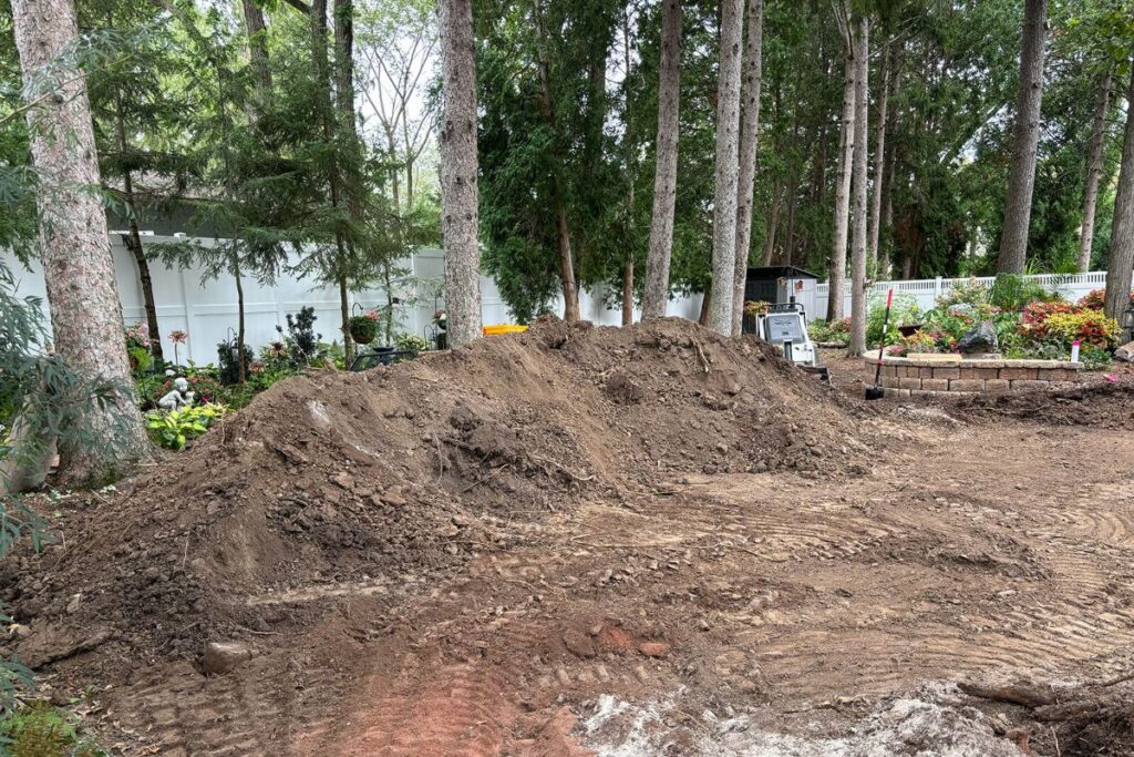 A large pile of excavated dirt in a backyard in New Berlin, Wisconsin, showing the initial stages of a patio and retaining wall project.