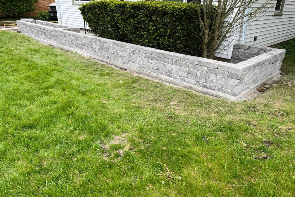 A newly constructed gray block retaining wall with a raised planting bed, installed in the front yard of a home in Milwaukee, WI.