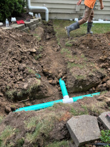 A view of a newly installed green drainpipe in a trench, part of a new drainage system for a home.