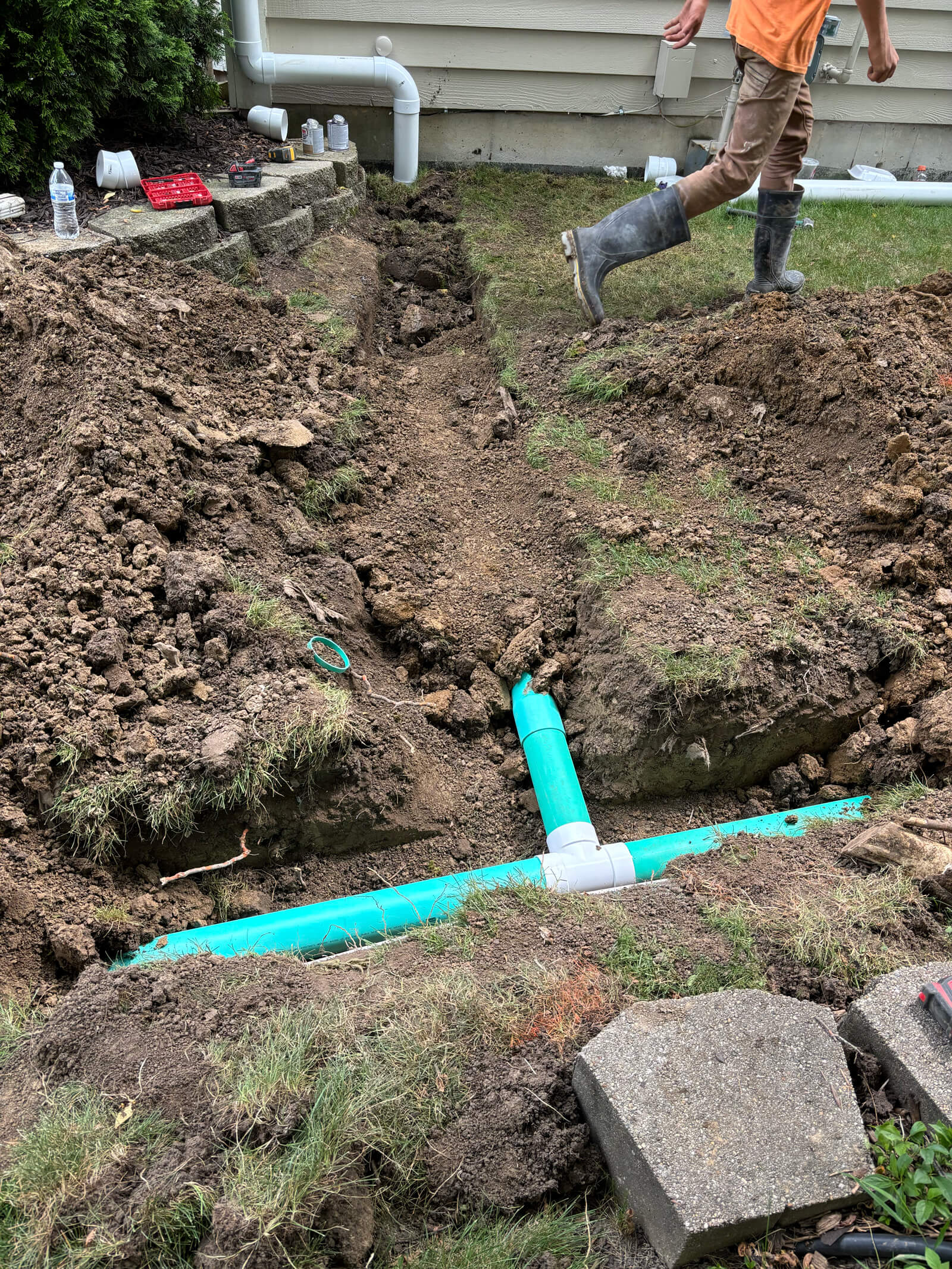 A view of a newly installed green drainpipe in a trench, part of a new drainage system for a home.