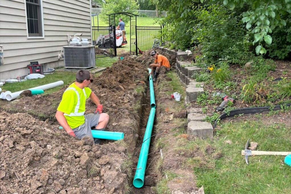 A crew from Concrete Landscape Solutions working on the installation of a new drainpipe in a trench behind a house.