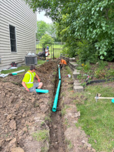 A crew from Concrete Landscape Solutions working on the installation of a new drainpipe in a trench behind a house.
