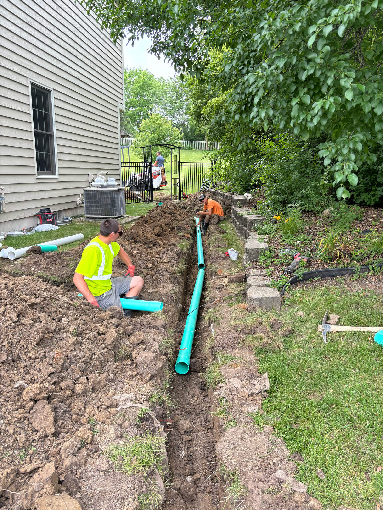 A crew from Concrete Landscape Solutions working on the installation of a new drainpipe in a trench behind a house.